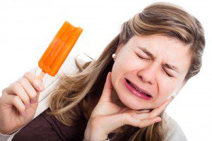 Woman holding a popsicle with a bite taken out of it, while holding her jaw and grimacing