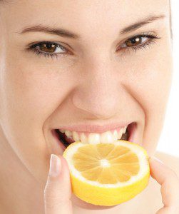 Young woman with nice teeth biting into a lemon