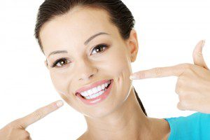 A smiling woman pointing to her perfect teeth on a white background