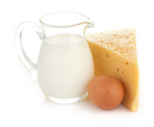 A glass pitcher of milk, an egg, and cheese on a white background