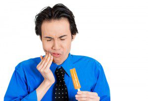 Portrait of a man putting his hand to his cheek from pain from frozen popsicle in his hand, isolated white background