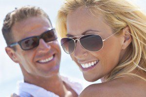 man and woman smiling with white smiles wearing sunglasses