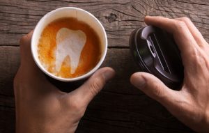 Paper cup of coffee is held by a man in his hand. Coffee makes teeth yellow and sick-img-blog