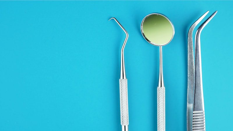 Professional dental tools against blue background: dental mirror, curved explorer, curved forceps.