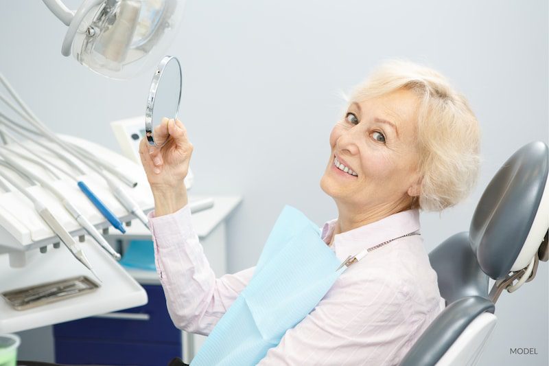 Older woman smiling in dental chair after looking at her new smile in the mirror.