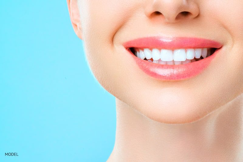 woman smiling with white teeth behind a blue background.