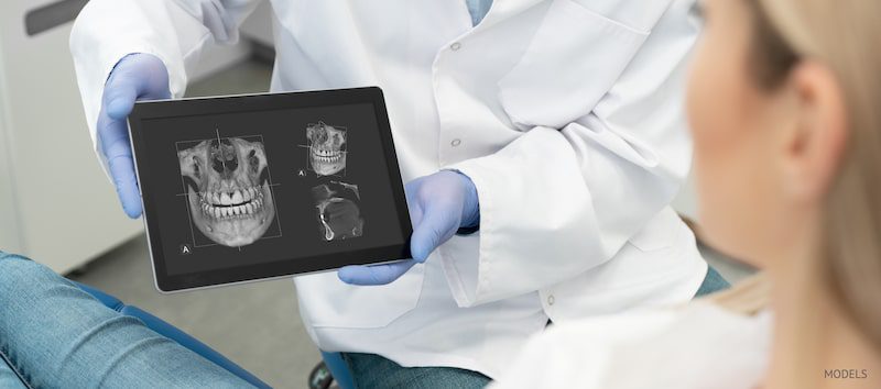 Dental patient sitting in the chair looking at x-rays of her dental structure.