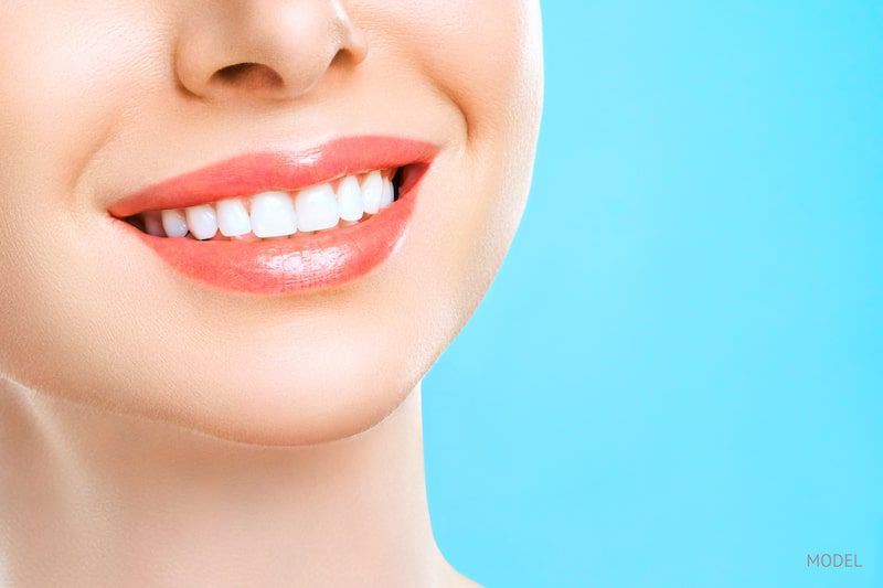 Young woman with healthy, white teeth smiling in front of a blue background.
