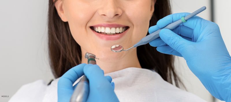Woman smiling at the dentist with dental tools near her mouth.