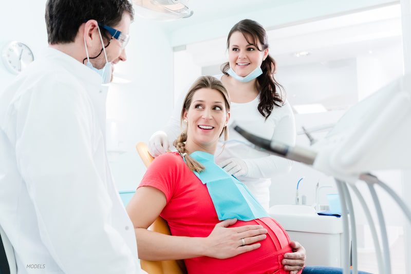 Pregnant woman sitting in a dentist office with dentist and nurse
