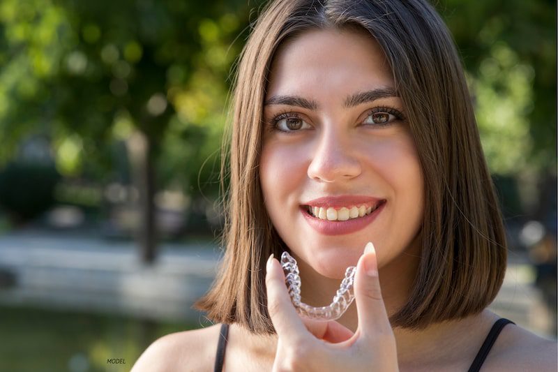Woman holding an invisible aligner, smiling.