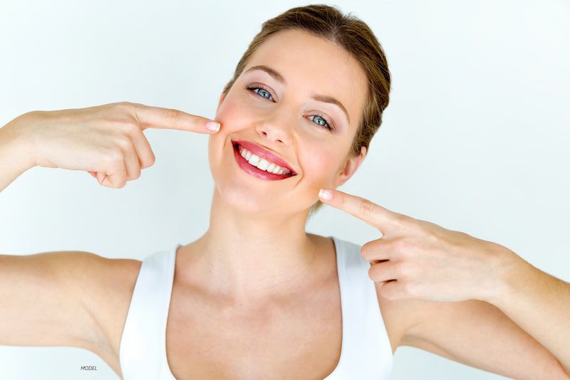 woman smiling, pointing at her teeth