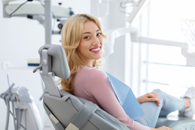 A woman with a bright smile sits in a dental chair.