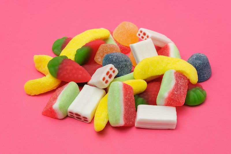 Colorful sticky jelly candies against a pink background.