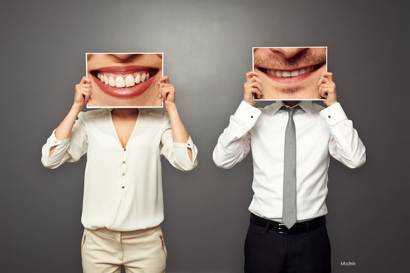 A woman and a man hold up large photos of smiles in front of their faces.