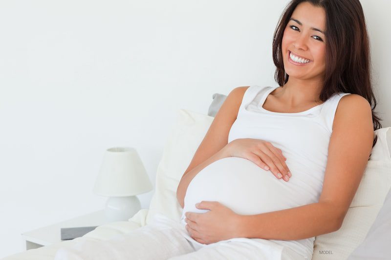 A pretty pregnant woman wearing white has beautiful teeth.