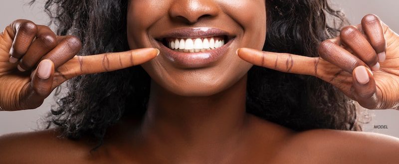 close up photo of Black woman with perfect teeth smiling and pointing at her smile.