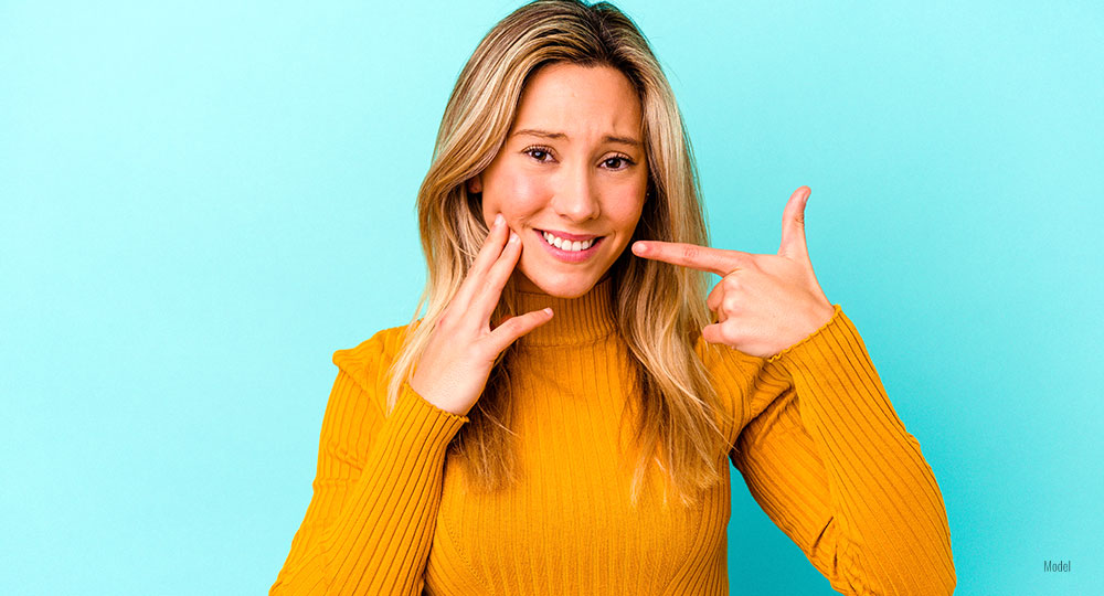  A woman wearing a yellow sweatshirt holds her jaw due to dental pain.